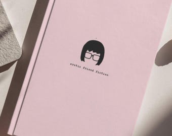 Op de afbeelding: Een lichtroze hardcover boek met een minimalistische zwarte afbeelding van een persoon met een bobkapsel en een bril. Onder de afbeelding staat de tekst "erotic friend fiction" gedrukt in een eenvoudig, zwart lettertype in typemachinestijl.