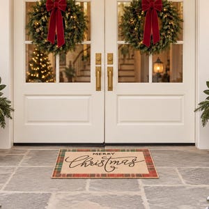 May include: A rectangular doormat with a tan center and a red and green plaid border. The text Merry Christmas is printed in black script in the center. The mat is placed on a stone porch in front of double white doors with wreaths.