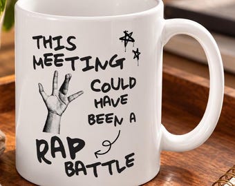 Op de afbeelding: Een witte keramische mok met zwarte tekst die luidt: "THIS MEETING COULD HAVE BEEN A RAP BATTLE". Het ontwerp bevat een zwart-wit afbeelding van een hand die een Vulcan-groet brengt en twee kleine handgetekende sterren.