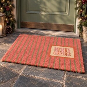 May include: A rectangular doormat with a textured surface featuring vertical red and green stripes. A central rectangular cream-colored patch displays the text MERRY CHRISTMAS in red and pink lettering. The mat has a coarse, fibrous appearance.