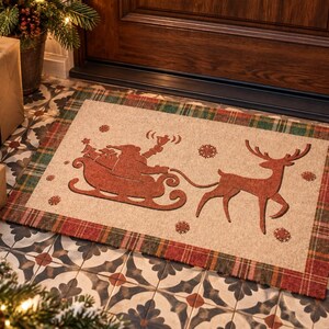 K&ouml;nnte beinhalten: Eine rechteckige Fu&szlig;matte mit beigefarbener Mitte, die eine dunkelrote Silhouette des Weihnachtsmanns im Schlitten, gezogen von einem Rentier, zeigt, umgeben von Schneeflockensymbolen. Die Matte hat einen rot-gr&uuml;n karierten Rand.