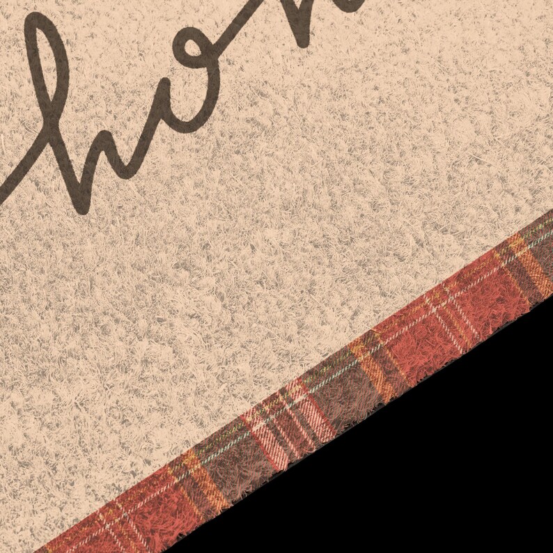 Puede incluir: Un felpudo beige texturizado que muestra una parte de la palabra home en letra cursiva marr&oacute;n oscuro. La esquina inferior derecha de la alfombra est&aacute; acentuada con un borde diagonal de tela con un patr&oacute;n de cuadros rojo, marr&oacute;n y naranja.