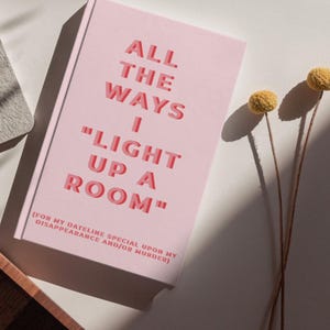 Op de afbeelding: Een roze notitieboek met de tekst "ALL THE WAYS I LIGHT UP A ROOM" in rode letters. Het notitieboek bevat ook de tekst "(FOR MY DATELINE SPECIAL UPON MY DISAPPEARANCE AND/OR MURDER)". Twee gele gedroogde bloemen staan op de achtergrond.