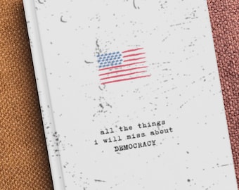 Op de afbeelding: Een wit notitieboek met een Amerikaanse vlag en de tekst "all the things I will miss about DEMOCRACY." Het notitieboek heeft een vintage uitstraling.