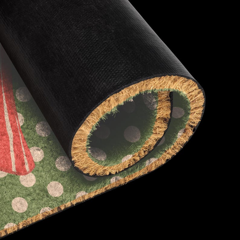 May include: A rolled doormat with a black rubber backing and a natural coir fibre front. The visible surface features a green background with a pattern of light-coloured polka dots and a portion of a red graphic design on the left side.