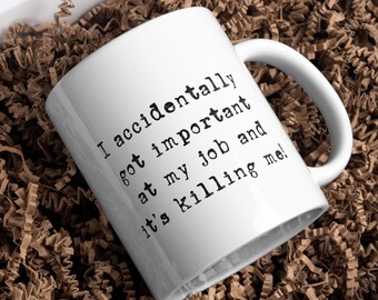 Op de afbeelding: Een witte keramische mok met zwarte tekst in typemachine-stijl die luidt: I accidentally got important at my job and it's killing me! De mok heeft een gebogen handvat en een gladde, glanzende afwerking met een eenvoudig, functioneel ontwerp.