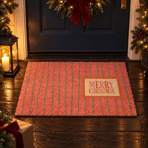 May include: A rectangular doormat with a textured surface featuring a red background and thin vertical green stripes. A light-colored rectangular patch on the right side displays the text Merry Christmas in a bold, dark red serif font.