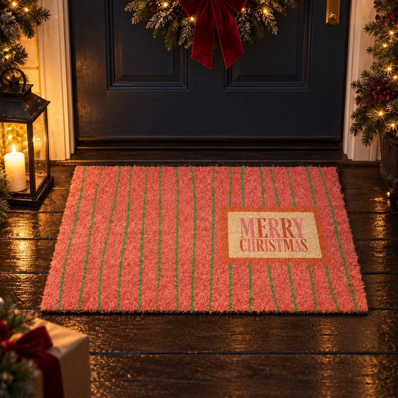 May include: A rectangular doormat with a textured surface featuring a red background and thin vertical green stripes. A light-colored rectangular patch on the right side displays the text Merry Christmas in a bold, dark red serif font.
