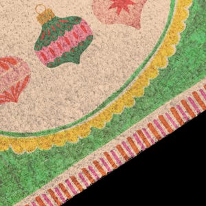 May include: A textured coir doormat featuring a beige background with printed Christmas ornaments in green, pink, and red. The border consists of a scalloped yellow trim followed by a wide green band and a striped edge in orange and pink.