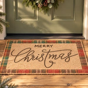 May include: A rectangular coir doormat featuring a central tan surface with the text Merry Christmas in dark brown script and block lettering. The mat is framed by a red, green, and brown plaid border pattern, creating a festive appearance.