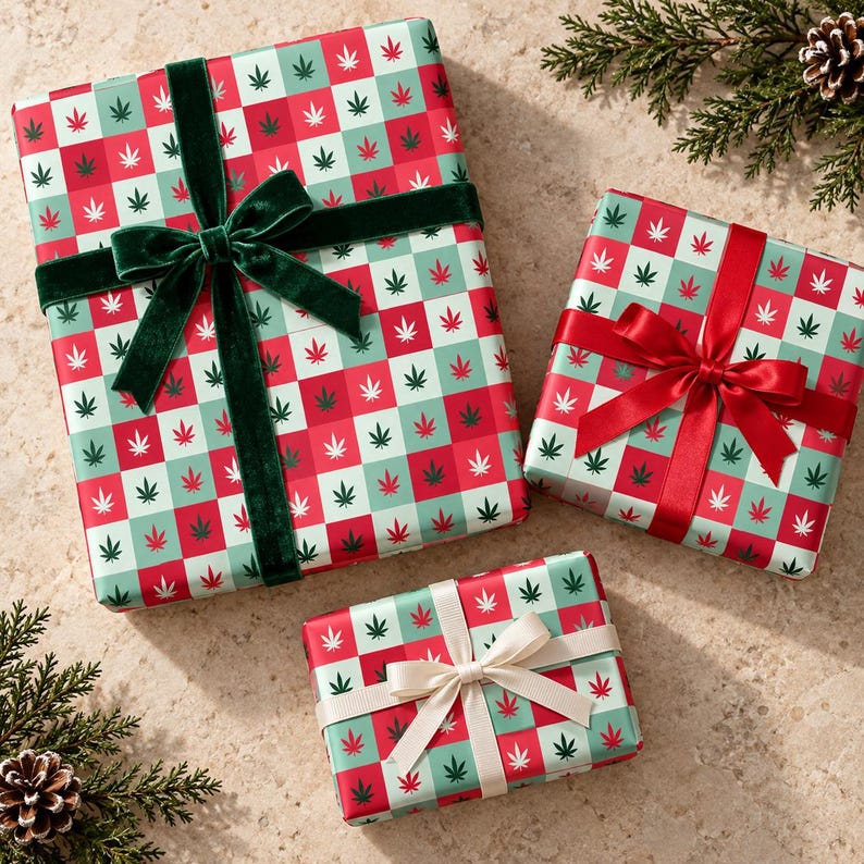 May include: Three rectangular gift boxes wrapped in paper featuring a red and light green checkered pattern with small white and dark green cannabis leaf icons. The largest box has a dark green velvet ribbon, the medium has a red satin ribbon, and the smallest has a cream-coloured ribbon.