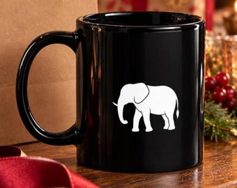Op de afbeelding: Een glanzende zwarte keramische mok met een eenvoudige witte silhouet van een olifant in profiel. De mok heeft een groot, gebogen handvat aan de linkerkant en een glad, cilindrisch lichaam. De witte olifantafbeelding staat in het midden.