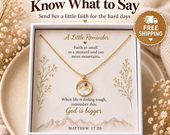 Op de afbeelding: Een goudkleurige ketting met een ronde hanger met een bergsilhouet en een kleine bruine kraal, gepresenteerd in een witte doos met de tekst A Little Reminder, Faith as small as a mustard seed can move mountains, en God is bigger.