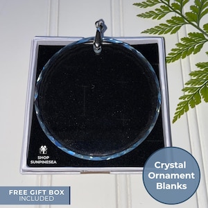 May include: A clear, faceted crystal ornament blank with a silver-colored metal loop, presented in a white gift box with a black velvet interior. The text "SHOP SUNPINESEA" and "FREE GIFT BOX INCLUDED" are visible.
