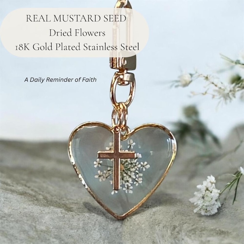 May include: A heart-shaped pendant featuring real mustard seeds and dried flowers encased in clear resin with an 18K gold-plated stainless steel frame and a small cross charm. The text reads: REAL MUSTARD SEED, Dried Flowers, 18K Gold Plated Stainless Steel, A Daily Reminder of Faith.