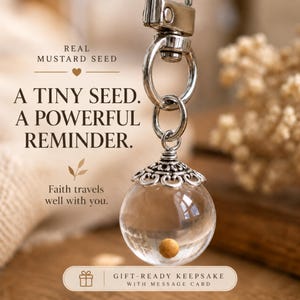 May include: A silver-toned keychain featuring a clear glass orb pendant with a single mustard seed inside. The pendant has an ornate silver cap and is attached to a metal ring. Text reads: REAL MUSTARD SEED, A TINY SEED. A POWERFUL REMINDER. Faith travels well with you. GIFT-READY KEEPSAKE WITH MESSAGE CARD.