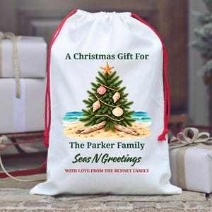 May include: A white drawstring gift bag with red cords featuring a printed Christmas tree decorated with seashells and a starfish on a sandy beach. The text reads: A Christmas Gift For The Parker Family, Seas N Greetings, WITH LOVE FROM THE BENNET FAMILY.