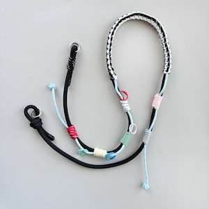 May include: A black and white braided rope leash with colorful accents. The leash features a black main cord with light blue and red accents, and a braided white and black handle. The leash has metal rings at the ends.