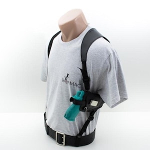 Puede incluir: Una funda de hombro de cuero negro con una bolsa negra y una pistola de color turquesa. La funda se lleva sobre una camiseta gris con el texto "B MAC" y un cinturón negro con hebilla plateada.