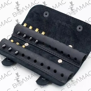 May include: Black leather ammunition holder, open to display several brass and black bullets. The holder is folded open, revealing multiple rows of ammunition. The leather is textured and has a matte finish. The brand name "VOLMAC" is visible.