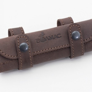 Puede incluir: Una funda de cuero marrón con cierre de presión y la palabra "BOMMAC" grabada en la parte delantera.