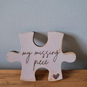 May include: A light-coloured wooden jigsaw piece with the words "my missing piece" in cursive script. A small heart is etched on the bottom right. The piece is displayed on a wooden surface.