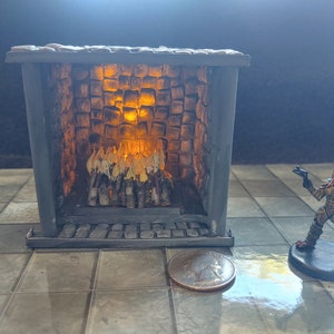 May include: A miniature stone fireplace with a glowing orange fire inside. The fireplace is made of gray stone and has a black metal grate. The fire is made of small sticks and is surrounded by a brick wall.