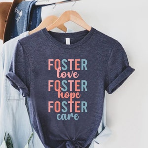 May include: A navy blue t-shirt with the text "FOSTER love FOSTER hope FOSTER care" in pink and blue lettering.