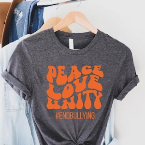 May include: A dark gray t-shirt with a bright orange graphic that says "Peace Love Unity" and the hashtag "#EndBullying".