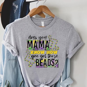 May include: Gray t-shirt with the text "Does your mama know how you got those beads?" in purple, yellow, and green boxes with purple, yellow, and green beads around the text.