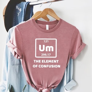 May include: A pink t-shirt with a white graphic of a periodic table element called "Um" with the atomic number 121 and atomic weight 298.17. The text "The Element of Confusion" is below the graphic.