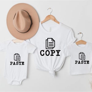 May include: White t-shirts with the words "COPY" and "PASTE" and a file icon. A white baby onesie with the words "PASTE" and a file icon.