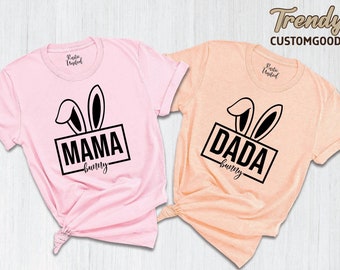 May include: Two pink and peach t-shirts with black bunny ears and text. The pink shirt says "Mama bunny" and the peach shirt says "Dada bunny".