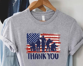 May include: Gray t-shirt with a distressed American flag design and five silhouetted soldiers standing in front of it. The text "THANK YOU" is printed below the flag.