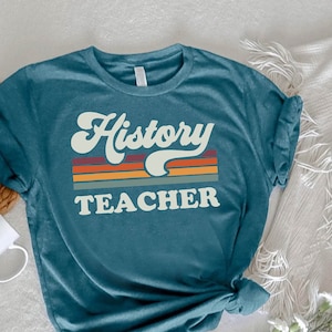 May include: Teal blue t-shirt with the text "History Teacher" in a retro font with a rainbow stripe design.