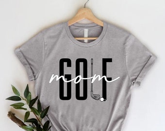 May include: Gray t-shirt with black text that reads "golf mom" and a black and white illustration of a golf club and ball.