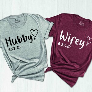 May include: Two gray and maroon t-shirts with the words "Hubby" and "Wifey" and the date "6.27.20" printed on them.