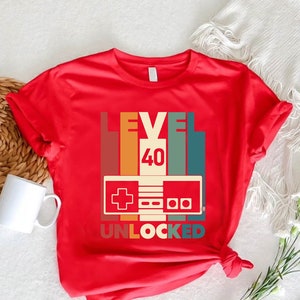 May include: Red t-shirt with a retro-style video game controller graphic and the text "Level 40 Unlocked".