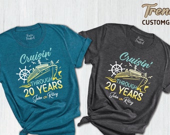 Puede incluir: Dos camisetas, una azul verdosa y otra gris, con un gráfico de un crucero y el texto "Cruisin' Through 20 Years". El texto "John Riley" también está incluido en las camisetas.