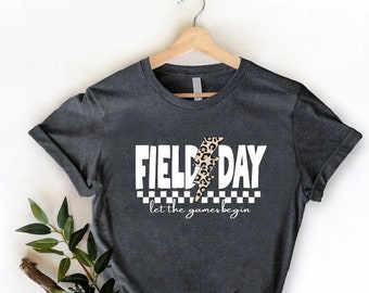 May include: A dark grey t-shirt with a white graphic that says "Field Day" with a leopard print lightning bolt in the middle. The text "let the games begin" is below the graphic.
