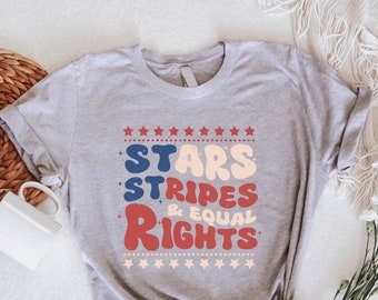 May include: A gray t-shirt with a red, white, and blue graphic that says "Stars Stripes & Equal Rights". The graphic is in a retro font style and is surrounded by stars.