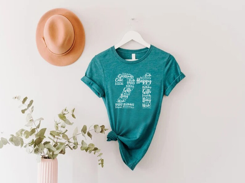 May include: Teal t-shirt with a white design of the number 21 made up of words related to birthdays, such as "Happy", "Cake", "Gifts", and "Friends".