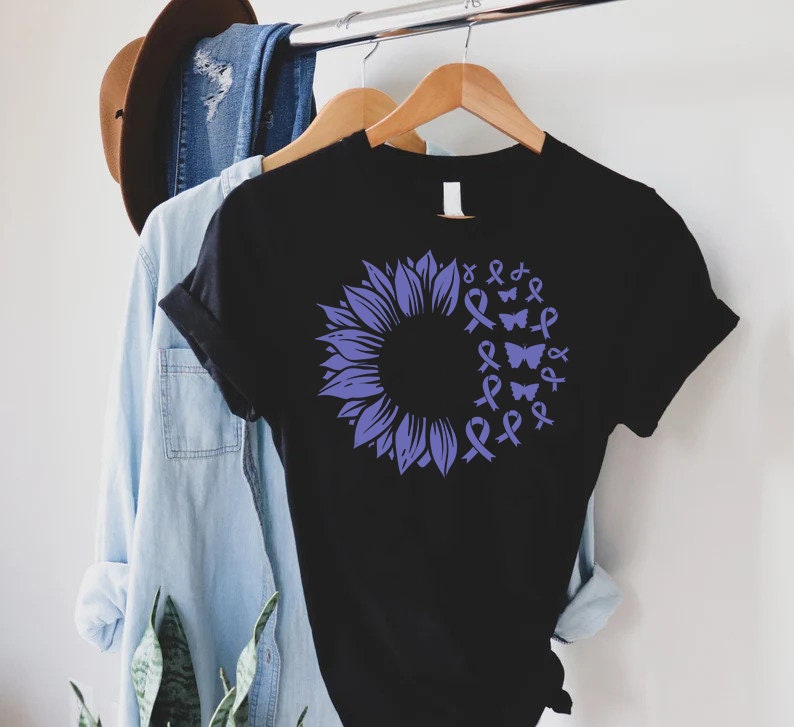 May include: Black t-shirt featuring a purple sunflower design. The sunflower is made up of purple ribbons and butterflies.
