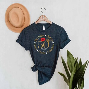 May include: A dark gray t-shirt with a gold glitter design that says "Birthday Queen 50 Sassy Classy Fabulous" with a red lip and crown graphic.