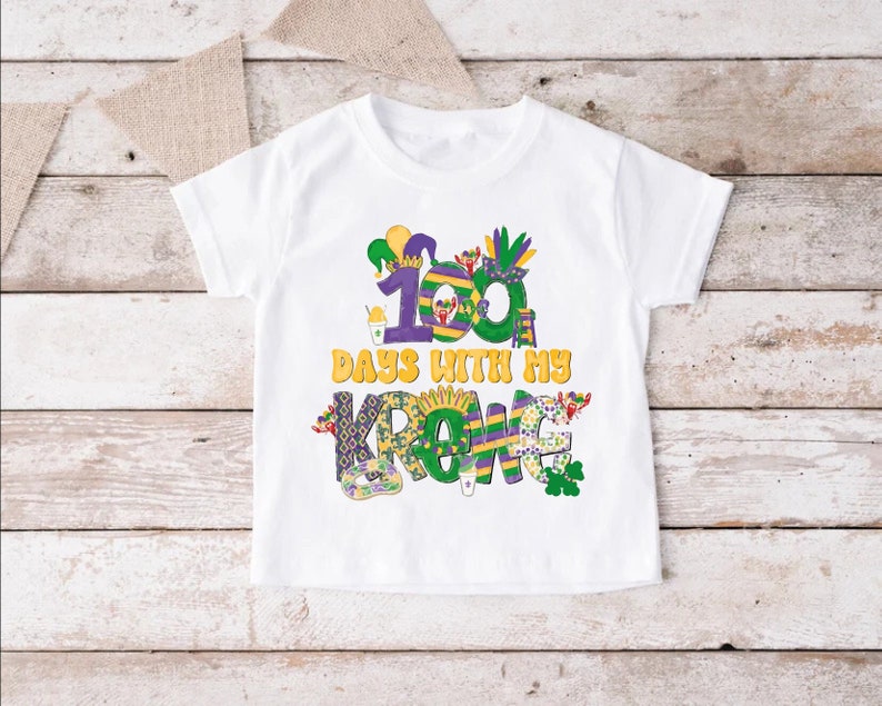 May include: White t-shirt with a colourful design featuring the text "100 Days With My Krewe". The design includes Mardi Gras themed elements like beads, masks, and a jester hat.