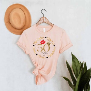 May include: Pink t-shirt with a gold glitter design that says "Birthday Queen 50 Sassy Classy Fabulous" with a red lip and crown graphic.