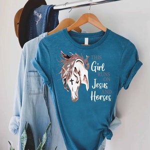 May include: Teal blue t-shirt with a white horse head graphic and the text "This Girl Runs On Jesus And Horses".