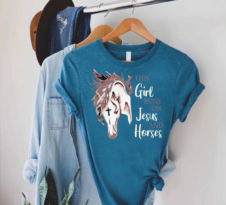May include: Teal blue t-shirt with a white horse head graphic and the text "This Girl Runs On Jesus And Horses".