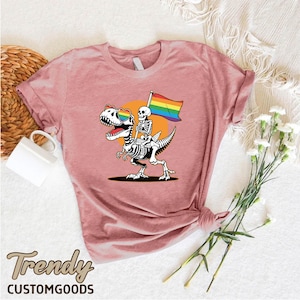 a pink shirt with a skeleton holding a rainbow flag