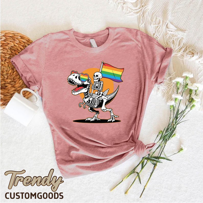 a pink shirt with a skeleton holding a rainbow flag